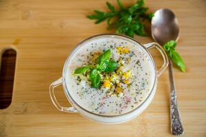 Cold soup with cucumbers, eggs, vegetables, yogurt and fresh herbs in a glass bowl . photo