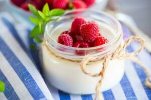 Sweet cooked homemade yogurt with fresh raspberries in a glass jar. photo