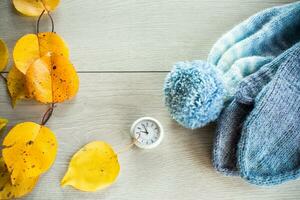 Autumn foliage, winter mittens and a clock on a wooden table. photo