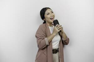 despreocupado asiático mujer es teniendo divertido karaoke, canto en micrófono mientras en pie terminado blanco antecedentes foto
