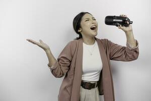 Carefree Asian woman is having fun karaoke, singing in microphone while standing over white background photo