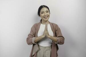 A smiling young Asian woman employee wearing a cardigan gestures a traditional greeting isolated over white background photo