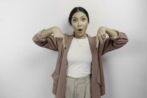 Shocked Asian woman employee wearing a cardigan pointing at the copy space below her, isolated by a white background photo