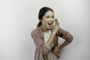 A young beautiful Asian woman employee wearing cardigan is shouting and screaming loud with a hand on her mouth, isolated by white background. photo