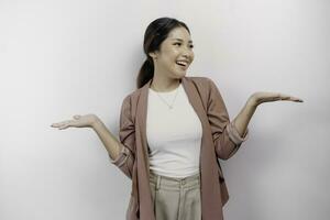 Excited Asian woman employee wearing cardigan pointing at the copy space beside her, isolated by white background photo