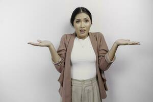 A thoughtful Asian woman employee wearing a cardigan is pointing to copy space beside her, looks so confused between choices, isolated by a white background photo