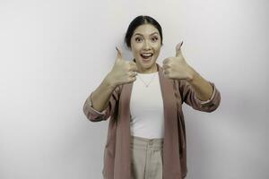 Excited young Asian woman employee is gesturing thumbs up for approval, isolated by white background photo