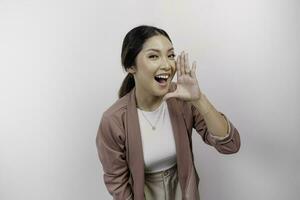 A young beautiful Asian woman employee wearing cardigan is shouting and screaming loud with a hand on her mouth, isolated by white background. photo