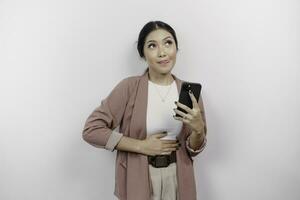 A hungry Asian woman employee is holding her phone and imagining yummy food she wants to order, isolated on white color background. photo