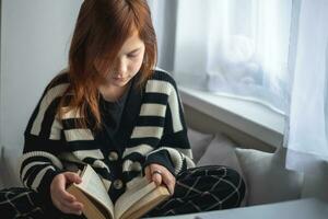 Teenage girl reading a book at home by the window photo