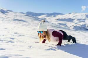 Woman in goggles in yoga pose on snowy plain photo