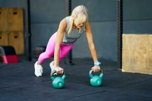 Focused young woman doing push ups with kettlebells in fitness gym photo