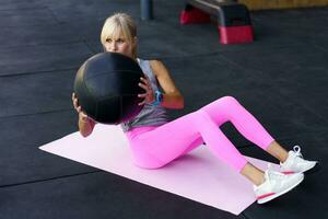 deportista haciendo ejercicios con medicina pelota en estera en gimnasio foto