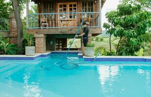 mantenimiento hombre limpieza nadando piscina con vacío succión manguera. trabajador limpieza un hermosa nadando piscina con succión manguera foto