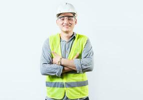 Portrait of handsome and smiling engineer with crossed arms isolated. Portrait of a young cheerful engineer in helmet and vest isolated. photo