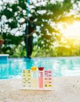 Water PH tester kit on the edge of the swimming pool with maintenance person in the background photo