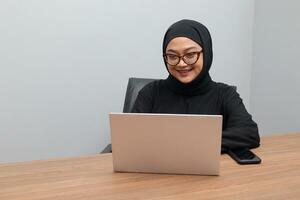 retrato de atractivo asiático hijab mujer trabajando en su ordenador portátil. musulmán niña haciendo tarea en oficina. empleado y Lanza libre trabajador concepto. foto
