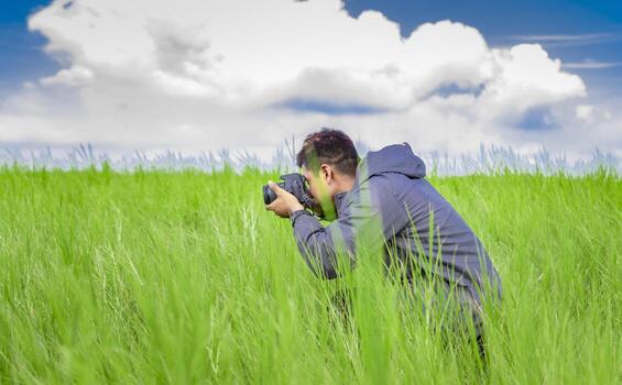 Man taking picture with camera in the field, photographer in the field taking a picture, Latino man in a green field taking a picture photo