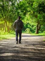 Man walking down a desolate road, man walking backwards on a road surrounded by vegetation photo