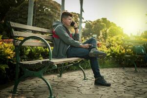 Man sitting on a bench calling on the phone, young man sitting on a bench with cell phone, close up of a young man calling on the phone sitting on a bench photo