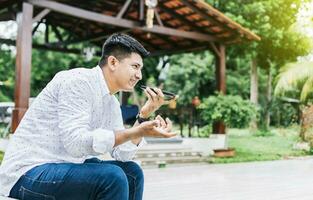 Man sitting sending a voice message with his phone and gesturing with his hands. Handsome man sitting outside sending a voice message with his cell phone, Guy sitting calling on the phone outside photo