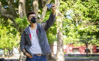 young man with mask taking a selfie, young man taking a selfie, man in jacket and mask taking a selfie photo