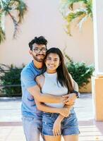 Portrait of a happy couple man hugging his girlfriend from behind, Portrait of a young couple man hugging his girlfriend from behind outside. Happy couple embracing looking at the camera photo