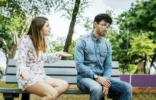 Upset couple arguing in a park. Girl arguing with her boyfriend sitting in a park, Young couple arguing and complaining sitting on a park bench, Concept of couple problems and jealousy photo
