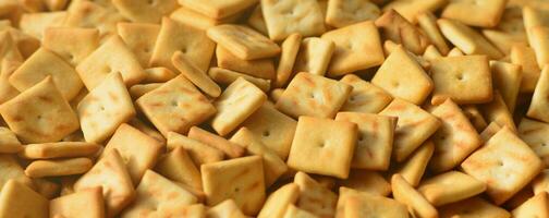 A lot of small cookies are square shaped. A pattern of a yellow salt cracker. Background image with salted pastry photo