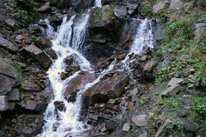 A mountain waterfall flows over the rocks. Waterfall cascade on mossy rocks photo