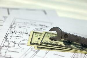 Spanner on top of money with blueprints of residential house plan. Restoring, repair, service maintenance cost photo
