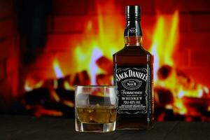 KYIV, UKRAINE - MAY 4, 2022 Jack Daniels original alcohol bottle on wooden table with red fireplace photo