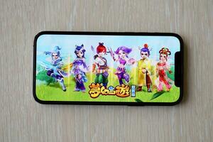 Fantasy Westward Journey mobile iOS game on iPhone 15 smartphone screen on wooden table during mobile gameplay photo