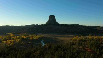 Teufel Turm Butte beim Sonnenuntergang im Herbst. Gelb und Grün Bäume. Gauner Bezirk. Wyoming, USA. Antenne Sicht. Drohne fliegt rückwärts und nach oben video