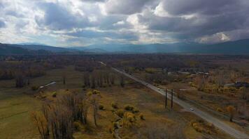 Cars on Moose-Wilson Road, Red Meadow and Mountains on Autumn Cloudy Day. Jackson Hole, Wyoming, USA. Aerial View. Drone Flies Forward video