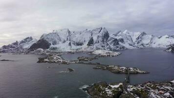 Hamnoy Village, Road and Mountains in Winter. Norwegian Sea and Stormy Sky. Moskenes, Lofoten Islands, Landscape of Norway. Aerial View. Drone Flies Backwards video