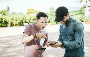 Two teenage guys checking their cell phones in the street, Two guys checking a cell phone outdoors, Two young men looking media on a cell phone in the street photo