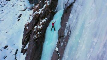 hielo alpinismo en congelado cascada. alpinista mujer es líder en hielo. aéreo De arriba hacia abajo vista. bareskoon valle, Kirguistán. zumbido moscas hacia abajo, inclinación arriba. grua Disparo video