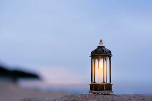 Islamic Lantern on rock with blurry sea beach background.Eid decorative traditional lamps illuminated ready for the Holy season of Ramadan Kareem,Eid Al fitr,Eid al Adha,Eid Mubarak,Muharram photo