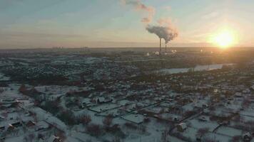 suburbano cabaña pueblo en Rusia a puesta de sol y térmico poder estación en invierno. aéreo vista. video