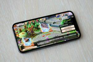 Fantasy Westward Journey mobile iOS game on iPhone 15 smartphone screen on wooden table during mobile gameplay photo