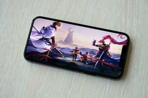 Honor of Kings mobile iOS game on iPhone 15 smartphone screen on wooden table during mobile gameplay photo