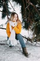 Teen blonde in a yellow sweater outside in winter. A teenage girl on a walk in winter clothes in a snowy forest photo