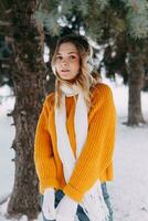 Teen blonde in a yellow sweater outside in winter. A teenage girl on a walk in winter clothes in a snowy forest photo