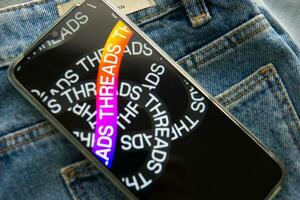 Tver, Russia - July 15, 2023, the threads logo on the smartphone screen lying on the jeans. The threads icon. The logo of the current application. Threads social network. photo