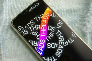 Tver, Russia - July 15, 2023, the threads logo on the smartphone screen lying on the jeans. The threads icon. The logo of the current application. Threads social network. photo