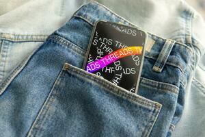 Tver, Russia - July 15, 2023, the threads logo on the smartphone screen lying on the jeans. The threads icon. The logo of the current application. Threads social network. photo