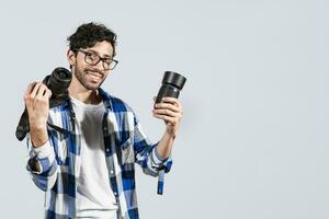 Portrait of smiling photographer man showing a camera and lens on isolated background. Smiling young man holding a camera isolated, Smiling photographer guy showing a camera and lens photo