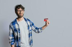 Person holding and looking at credit card with distrust, Confused handsome man holding credit card isolated. Insecure young man holding a credit card. Concept distrust with credit cards photo