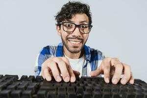 Portrait of nerdy man in front of keyboard, Cheerful nerdy guy with hands on keyboard. Funny nerdy person in front of the keyboard smiling at the camera photo